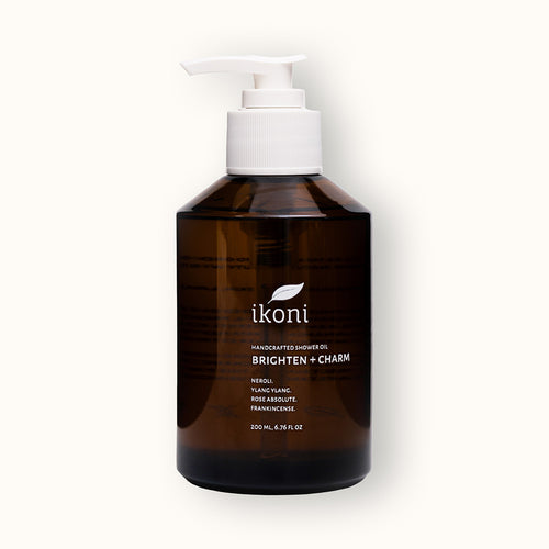 A brown glass bottle with white pump of ikoni Brighten + Charm shower oil.