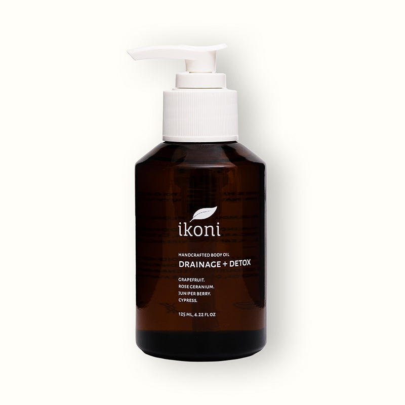 A brown glass bottle with white pump of ikoni Drainage + Detox body oil.