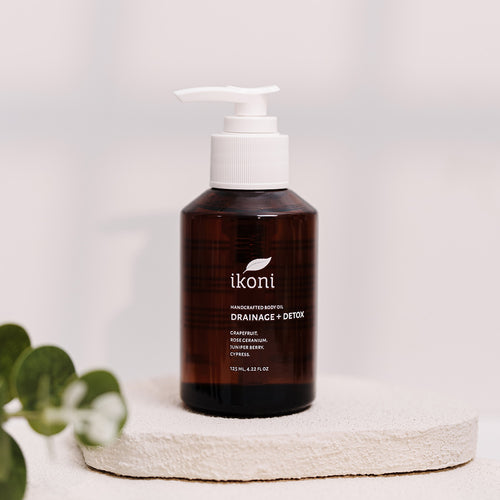 A brown glass bottle with white pump of ikoni Drainage + Detox body oil against an off-white background.