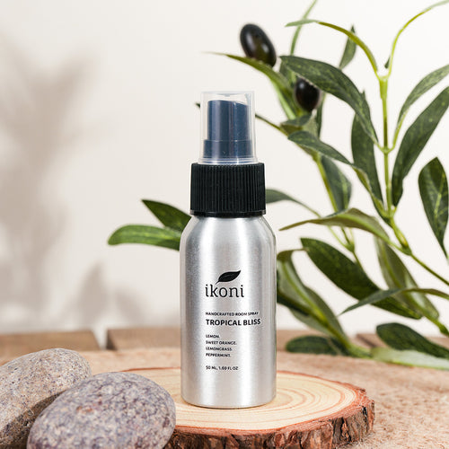 Polished metal spray bottle with black top of ikoni Tropical Bliss on a wooden surface with greenery in the background.