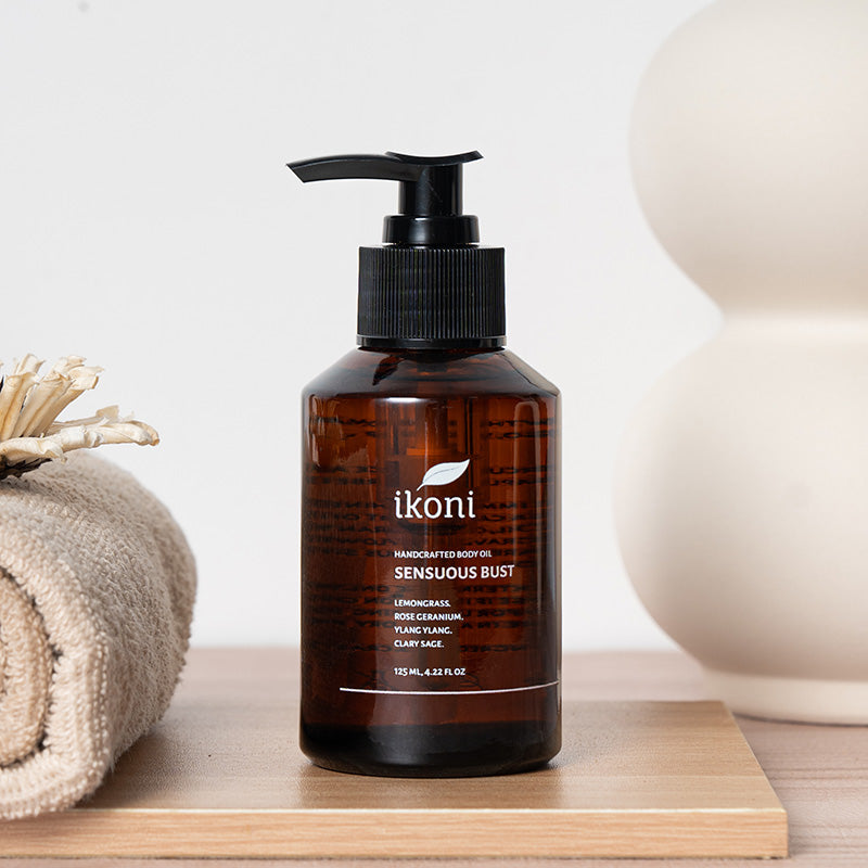 Brown bottle with black pump of ikoni Sensuous Bust body oil on a wooden surface and decorative elements.