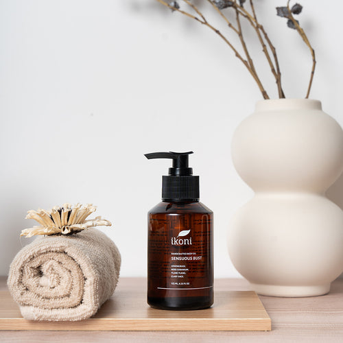 Brown bottle with black pump of ikoni Sensuous Bust body oil on a wooden surface and decorative elements.