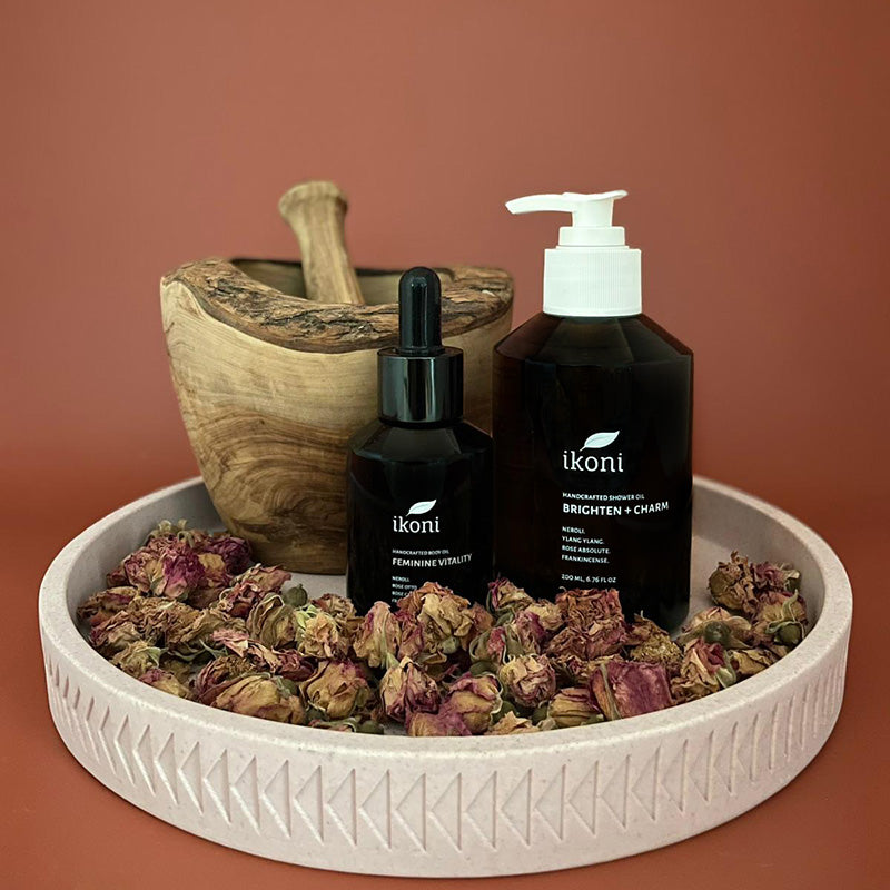Two ikoni products on a decorative tray with dried flowers and a wooden pestle against a brown background.