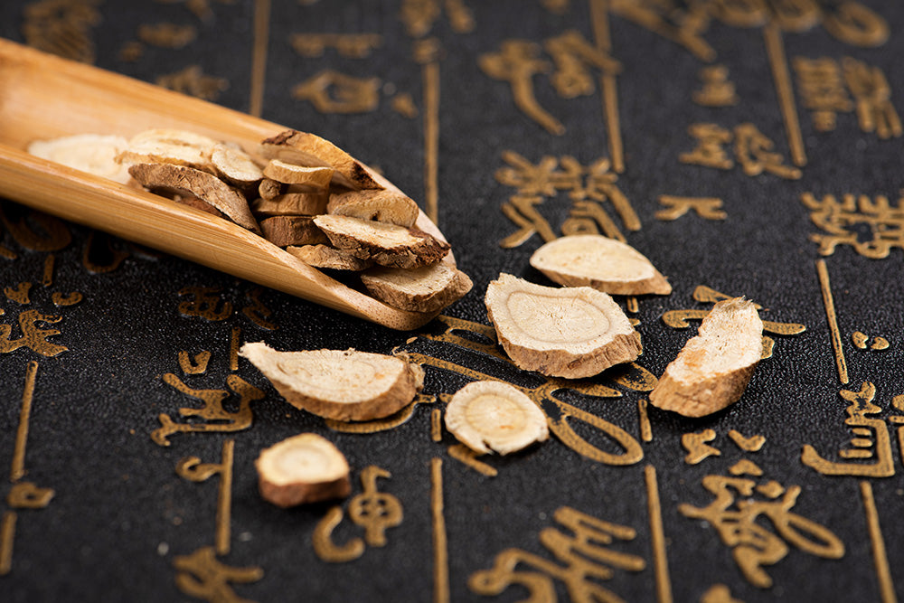 Dried roots on a wooden spoon against a black background with gold Chinese characters.