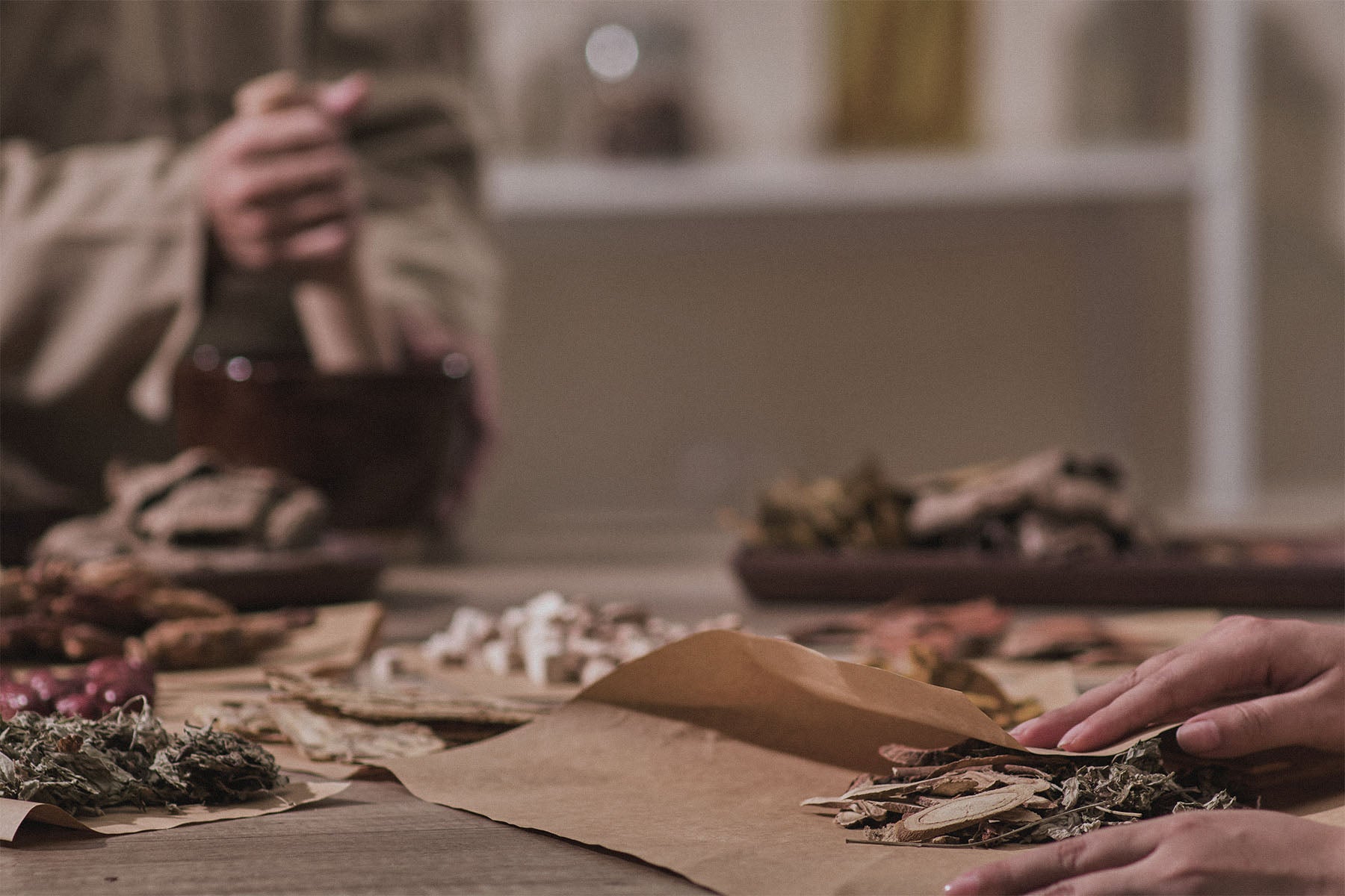 Person grinding dried Chinese herbs on a table with a blurred background.